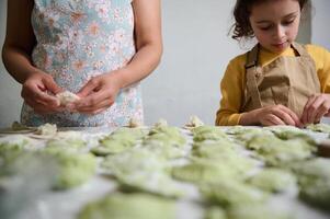 atención en moldeado hecho en casa empanadillas en enharinado mesa en contra el antecedentes de joven mamá y hija Cocinando juntos. Ravioles. pelmeni. varennyky relleno con machacado patatas foto