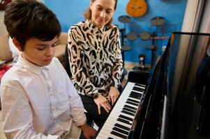 hermoso adolescente chico tomando piano lección, apasionadamente jugando el llaves debajo su del maestro guía, sensación el ritmo de música. musical educación y talento desarrollo en Progreso foto