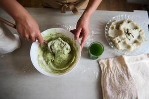 Directly above woman's hands using wooden spoon mixing ingredients and kneading dough for making homemade ravioli or dumplings stuffed with mashed potatoes, standing t kitchen table with ingredients photo