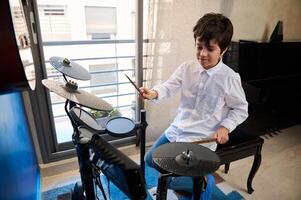 Teenager boy playing drums at home music studio, holding drumsticks and banging drums, beating on drum kit. Learning percussion musical instrument photo