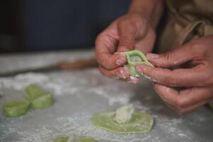 Close-up hands of a woman in the rural kitchen, sculpts dumplings from dough with mashed potatoes filling. Cooking delicious homemade vegetarian dumplings, Italian ravioli or Ukrainian varenyky photo