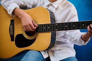 un niño mano punteo el instrumentos de cuerda mientras jugando el guitarra. chico aprendizaje a jugar el guitarra durante un música lección. foto