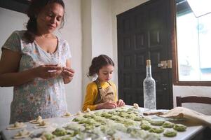 auténtico joven bonito mujer, madre y su pequeño niño, hija en el rural cocina, esculpir empanadillas desde masa con machacado patatas relleno. Cocinando delicioso hecho en casa vegetariano empanadillas foto