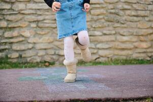 Details on legs of an active little child girl playing hopscotch, takes turns jumping over squares marked on the ground. photo