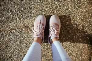 deportista punto de vista. piernas y pies de hembra atleta en elegante corriendo Deportes zapatos, rosado zapatillas en el asfalto foto