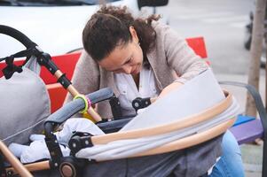 Happy young mother smiling looking at her baby sleeping in baby pram. Maternity leave. Motherhood. Childbirth concept photo