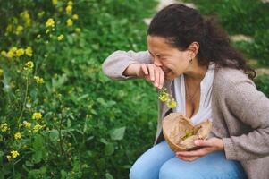 A young woman sneezing while gathering wildflowers in the meadow outdoors, suffering from allergy in the spring time photo