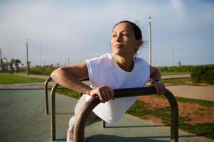 Athletic young woman in sportswear doing bar push-ups on cross bar, working out outdoors in the urban sportsground photo