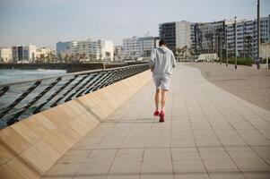 Rear view sportsman athlete running on a treadmill on the promenade in urban environment. Cardio workout. Sport. Fitness photo