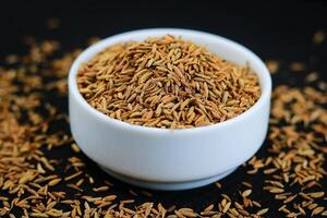 Cumin seeds in a white bowl on a black wooden table. photo
