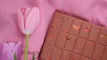 A bar of pink ruby chocolate with sublimated freeze-dried strawberries and almonds and spring tulip flowers . A dessert based on berries and nuts for International Women's Day, March 8, mother's day photo