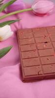 A bar of pink ruby chocolate with sublimated freeze-dried strawberries and almonds and spring tulip flowers . A dessert based on berries and nuts for International Women's Day, March 8, mother's day photo