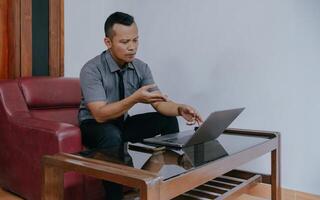 joven empresario enfocado trabajando en computadora portátil, utilizando vídeo llamada con cliente en ordenador portátil. joven indonesio hombre concentrando en dando en línea educación clase conferencias, consultante con clientes. foto