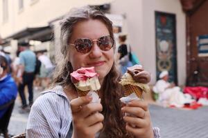 Konstanz, Baden-Wuerttemberg, Germany - June 5th 2023. Gelateria Da Toni. Teenage girl is holding 2 waffle cones, filled with traditional italian ice-cream gelato. Rosgartenstrasse on the background photo