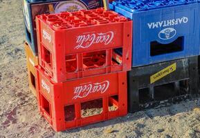 durres, albania septiembre, 3, 2022. coca reajuste salarial, schweppes, qafshtama el plastico vacío cajas con marca logos apilado en parte superior de cada otro en el arena playa detrás el café o restaurante exterior. foto