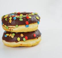 A stack of doughnuts glazed with chocolate and colorful smarties. Pile of 2 donuts isolated on a white background. Side view. Copy space photo