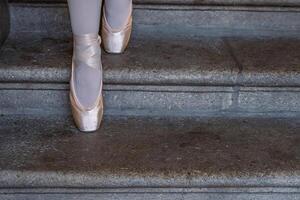 Closeup of ballerina's pointes on the gray stone steps background. Dance sitting on the steps. Ballerina feet with pink ballet slippers on. Minimalistic, simple. Copy space. photo