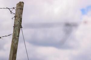 Grapevine wooden pole with guiding wires on cloudy sky background. Old wooden pillar in the vineyard. Low angle view. photo