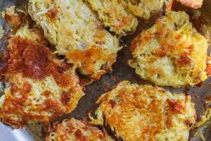 Homemade potato pancakes are being fried in an iron pan. Flipping the potato pancakes with the wooden paddle. Serving crispy gold brown draniki on the metal pan. Closeup. Top view photo