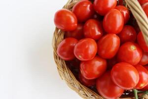 Many red cherry tomatoes with sepals in the basket isolated on the white background.  Tomato pile. Ripe and fresh organic vegetables harvested from local farmers. Clipping path. Top view. Copy space. photo