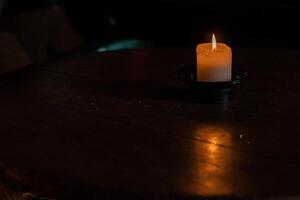 Beautiful burning wax candle with the flame reflection on the wooden table. Dark background with turquoise and blue reflex. Minimalistic concept. Graphic design, poster. Copy text space. Bokeh effect photo