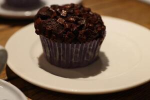 Chocolate muffin on the white plate.  Homemade Cupcake with chocolate chips on the wooden table in cafe. Delicious Brownie cake. Cozy atmosphere. Closeup. Side view photo