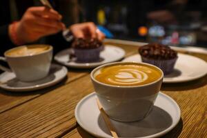 Copenhagen, Denmark - February, 20th, 2023. Espresso House. A cup of cappuccino with milk foam and delicious homemade chocolate cupcake on the vintage wooden table. Selective focus photo