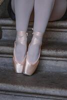 Closeup of ballerina's legs with her pink pointes shoes on. Ballet dancer is sitting on the gray stone steps. Dancer is resting on the stair. Dancers feet with pink ballet slippers on. photo