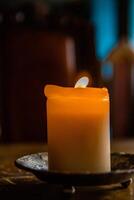 Lit candle on the wooden table. Burning candle in the candleholder. Burning light. hot fire. Cozy atmosphere. Selective focus. Backlight from the window. photo