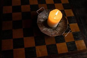 Lit candle on the wooden chessboard. Burning candle on the wooden table in the candleholder. Burning light. Cozy atmosphere. Copy Space. Backlight from the window. Top view. Selective focus. photo