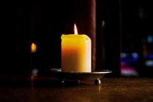 Lit candle on the wooden table. Burning candle in the candleholder. Burning light. hot fire. Cozy atmosphere. Selective focus. Backlight from the window. photo