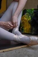 Close up of female ballet dancer putting on, tying ballet shoes. Adult ballerina sits on floor at dance studio and puts on pointe shoes before choreography lesson. Preparing to performance. photo