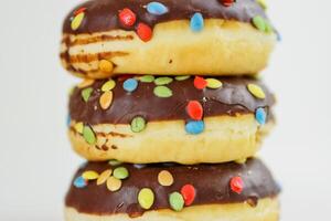 A stack of doughnuts glazed with chocolate and colorful smarties. Pile of 3 donuts isolated on a white background. Side view. Copy space photo