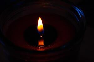 Beautiful burning candle with the flame reflection on the melted wax Closeup. Oil lantern. Blue splash on dark black background. Minimalistic concept. Graphic design, poster. Copy text space. Bokeh. photo