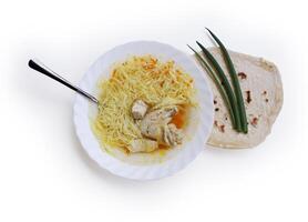 Delicious homemade chicken soup with vermicelli, carrots and chicken wing served in the white plate. Lavash and green onions. Top view. Cutout and isolated with clipping path on the white background photo