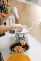 Housewife makes minced meat on an electric meat grinder pushing the meat in the tray with a pusher photo