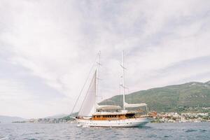 Luxury sailing yacht sails on the sea against the backdrop of green mountains photo