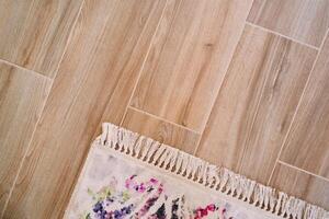 Corner of a colorful carpet with tassels lies on a wooden floor. Top view photo