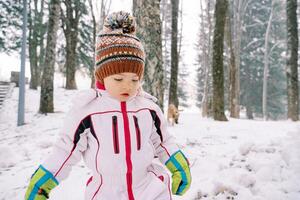 Little girl walks through a snowy forest and looks at her feet photo