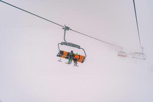 Skiers on a chairlift ascend a mountain through thick fog photo