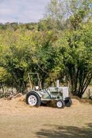 Small gray tractor stands on hay near green trees photo