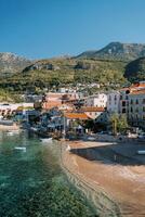 Colorful houses with red roofs on the seashore at the foot of the mountains. Przno, Montenegro photo