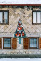 sintió Navidad árbol con rojo arcos y guirnaldas cuelga en el fachada de el casa foto