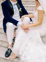 Bride and groom sit on old stone steps and place their hands on each other laps. Cropped. Faceless photo