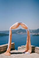 Wedding arch decorated with fabric stands on an observation deck above the sea photo