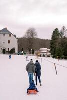 Mom and dad are carrying a small child on a sled climbing a hill. Back view photo