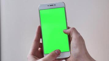 POV scrolling phone with green screen on white isolated background close-up in female hands. Modern technology in real life video