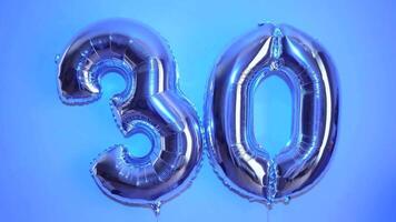 Two silver balloons in the shape of the number thirty 30 for a birthday anniversary. Close-up on a colored background video