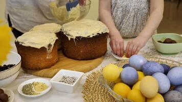 madre e sua figlia preparazione per Pasqua. il madre è mettendo glassatura su il torte, mentre il figlia è decorazione il Pasqua uova. Là siamo anche piatti di colorato uova, cioccolato caramelle video