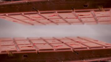 avvicinamento un' latte rubino cioccolato bar con pezzi di noccioline mandorle e fragola, visualizzato contro un' grigio sfondo è posto su un' riflessivo superficie, la creazione di un' rispecchiato Immagine di si video